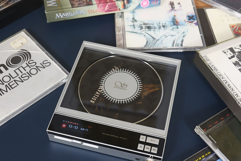 A Shanling CD player on a blue surface with several scattered CDs, including one titled "Monoliths & Dimensions."