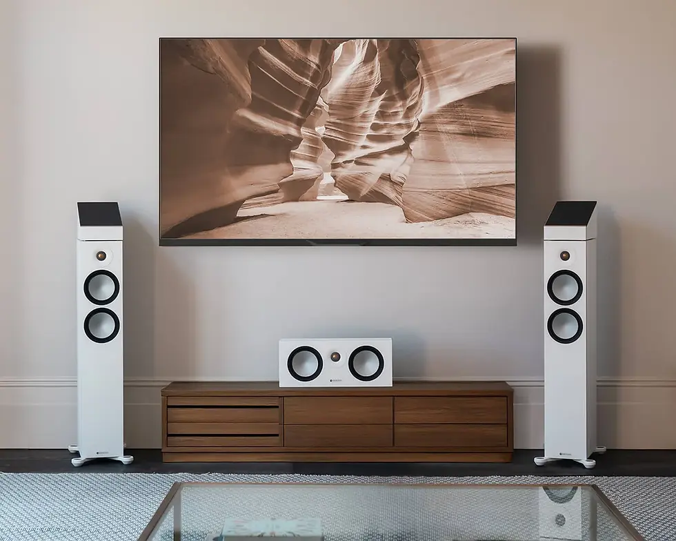 Home theater setup with a flat-screen TV displaying a canyon image. Two tall white speakers and a center speaker on a wooden console below.