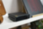Black AIYIMA A80 audio amplifier on a white shelf, next to a brown glass vase and a record with red zigzag patterns. Minimalist setting.