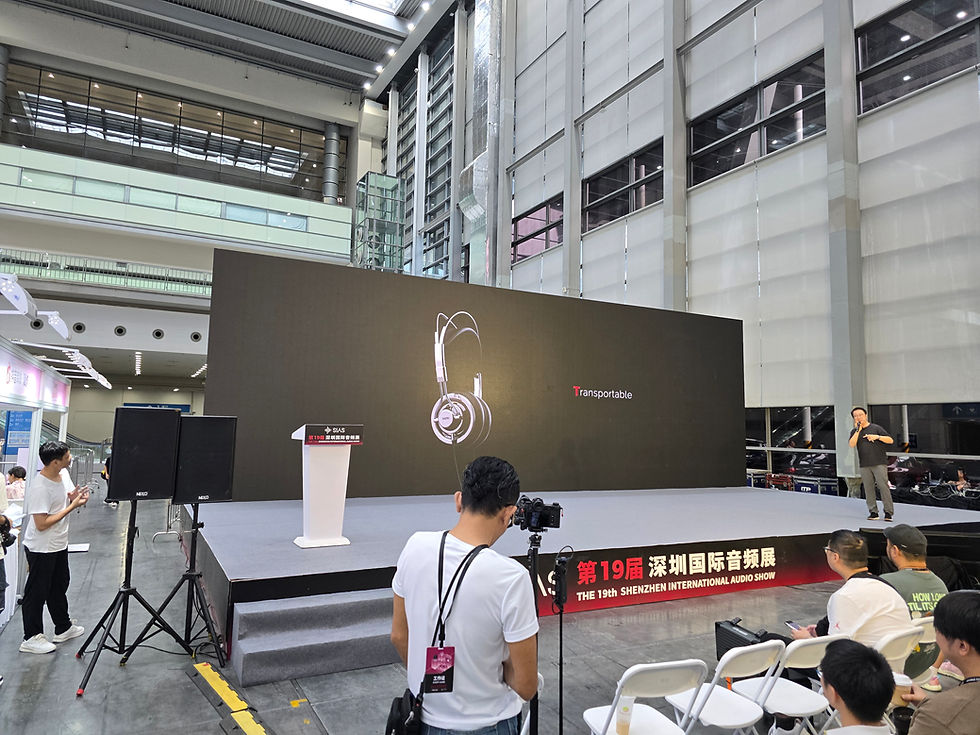 Speaker on stage at the 19th Shenzhen International Audio Show, large screen with headphones and "Transportable" text, audience seated.