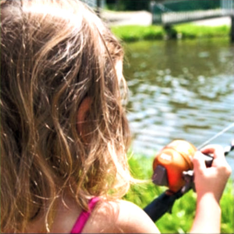 Enfant pratiquant la pêche à l'étang à la Pisciculture Denis Fournier, devant un étang de pêche récréative.