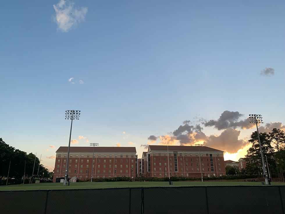 A residential building at USM behind the football practice field. The sky is blue with sparse clouds and the sun is setting