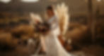 Bride in a lace dress holding a bouquet, standing in a desert with pampas grass and vases. Warm tones create a serene, romantic mood.