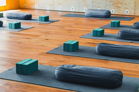 Blue yoga mats neatly aligned on a wooden floor, each with a support and two foam bricks.