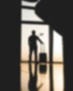 Silhouette of man with suitcase standing a window at sunrise watching a plane take off