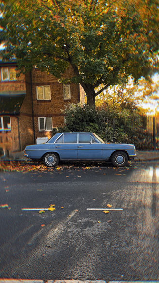 Blue vintage car parked under autumn tree on wet road