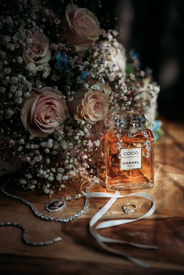 Chanel Coco perfume, wedding ring, and flowers on a table