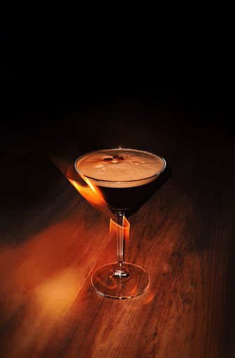 Martini glass with dark drink and flaming orange peel