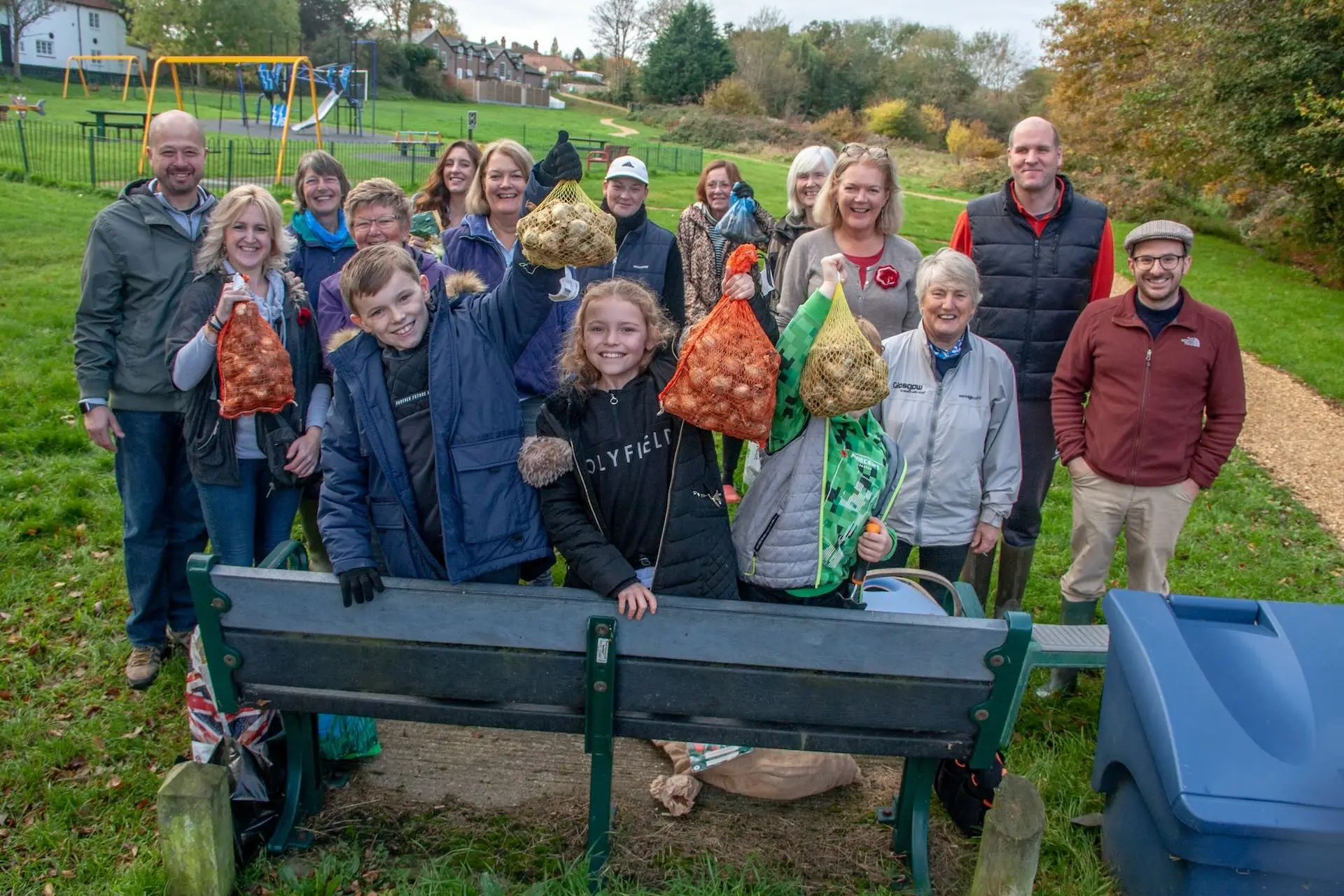 A group of children and adults smiling in a field holding bags of planting bulbs