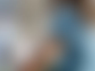 Woman in a blue shirt checks her phone's glucose monitoring app. A sensor is on her arm. She's indoors on a sofa with soft lighting.