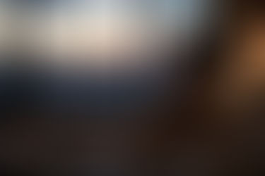 Person sitting quietly near a large window at dusk in a softly lit modern interior, reflecting the unfinished stillness and unresolved pacing explored in the article “When Nothing Fully Lands.”