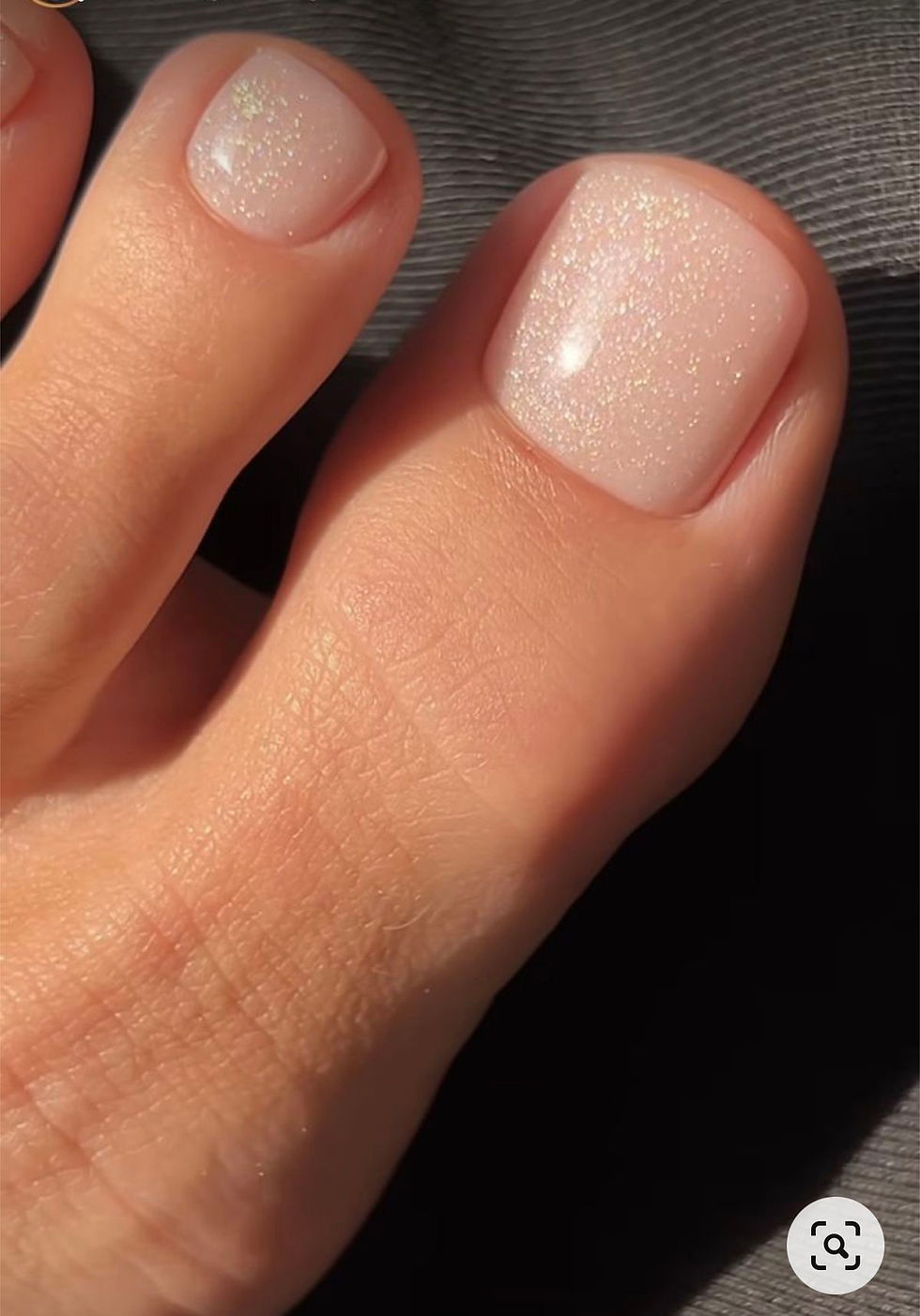 A close-up of a womans big toe her pedicure is sparkly pink