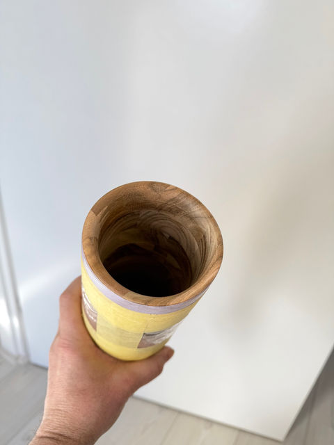 Hand houdt een houten vaas vast met gele tape. Vaas van tafelhout. Deur op achtergrond. binnenkant vaas