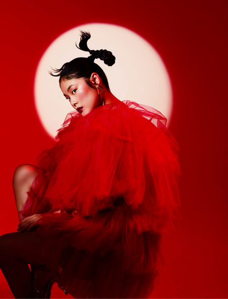 Fashion editorial at Pier 59 Studios featuring Chen Yu from Industry Model Management in a voluminous red tulle dress with a high-fashion hairstyle, set against a bold red background with a glowing spotlight effect.