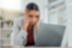 Business woman in gray blazer, with head in hands, looking at computer with a frustrated look.