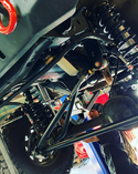 Mechanic working on off-road truck suspension and chassis, detailed view underneath.