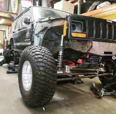 Black Jeep Cherokee XJ off-road build with custom suspension in garage.