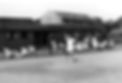 Old wooden clubhouse and shale courts with members outside the clubhouse in 1960.