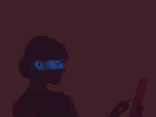 A woman holding and looking into an iPad with a blue light streak across her eyes.