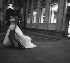 Schwarz-Weiß Bild der Braut in der Mailänder Innenstadt die Abends durch die Stadt rennt und man Ihre Lederstiefel sehen kann.