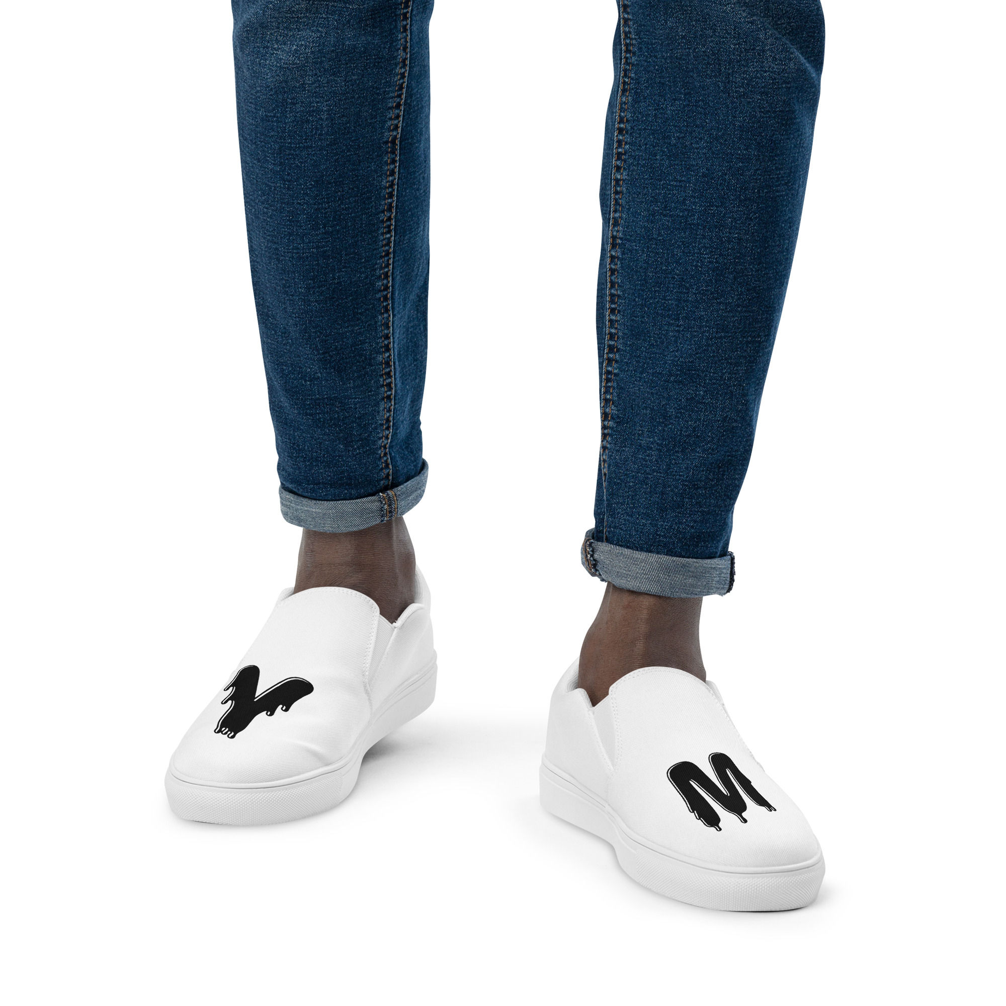Man modeling white canvas slip-on shoes with black letter M
