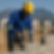 Builder in blue jacket and yellow hard hat laying bricks on a construction site with mountains in the background, under a clear sky.