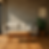 Beige sofa with cushion on wooden floor, potted plant to the right, framed art on wall. Sunlight casts shadows, creating a serene mood.