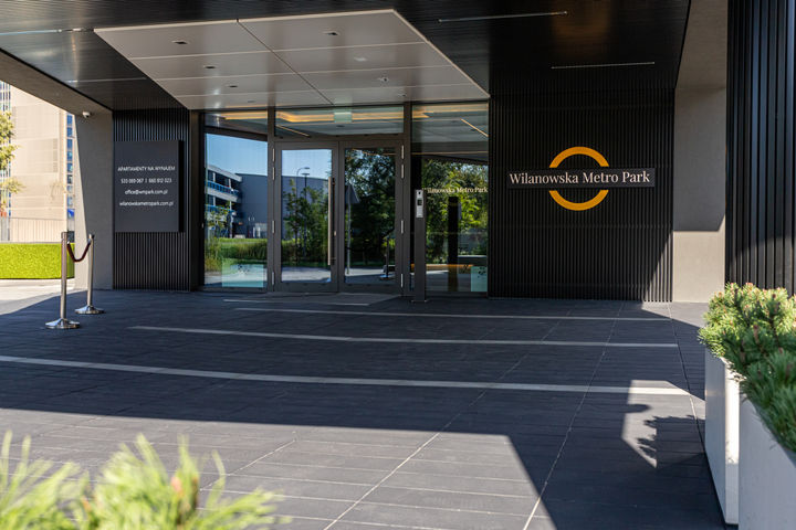 Luxury entrance of Wilanowska Metro Park with modern architectural design, dark textured panels, and sleek glass doors for a sophisticated urban residence.