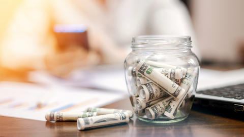 jar-with-rolled-banknotes-table-laptop-papers-woman-background.jpg