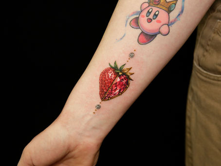Strawberry gemstone jewelry tattoo on forearm — realistic ruby pendant with gold setting and diamond chain dots, colour realism style by Wild Crane Tattoos Markham