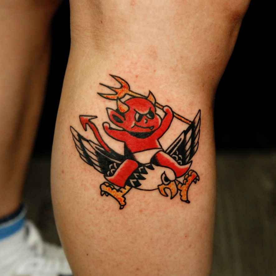 Old School American Traditional devil tattoo with wings and bold red, black, and grey linework on lower leg, by Ken at Wild Crane Tattoos Markham
