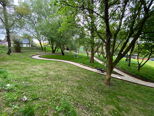 A winding path of white stone pebbles leads around an orchard of trees on a bank of grass.