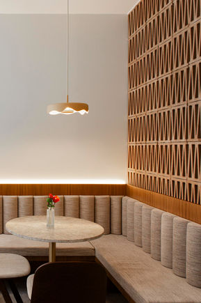 Warm horecainterieur met ronde tafels, maatwerkzitbanken en houten wandbekleding.