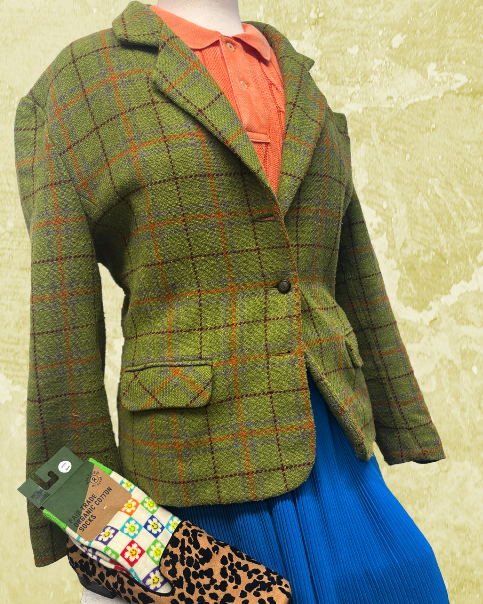 A photo of a khaki tartan blazer with an orange polo and blue skirt. To the left is a leopard print shoe with some checkered rainbow socks.