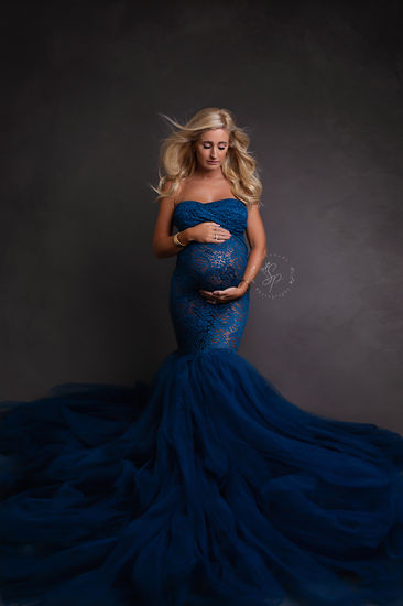 A stunning maternity portrait featuring a mother-to-be in a flowing royal blue gown, standing tall and gracefully embracing her pregnancy.