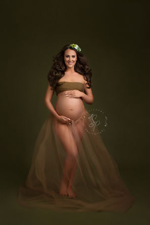A maternity portrait featuring an expectant mother in a warm, earthy-toned gown, with her hands gently cradling her baby bump, evoking a sense of calm and serenity.