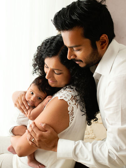 Family cuddling with newborn baby in neutral-toned photography studio using white and beige styling.