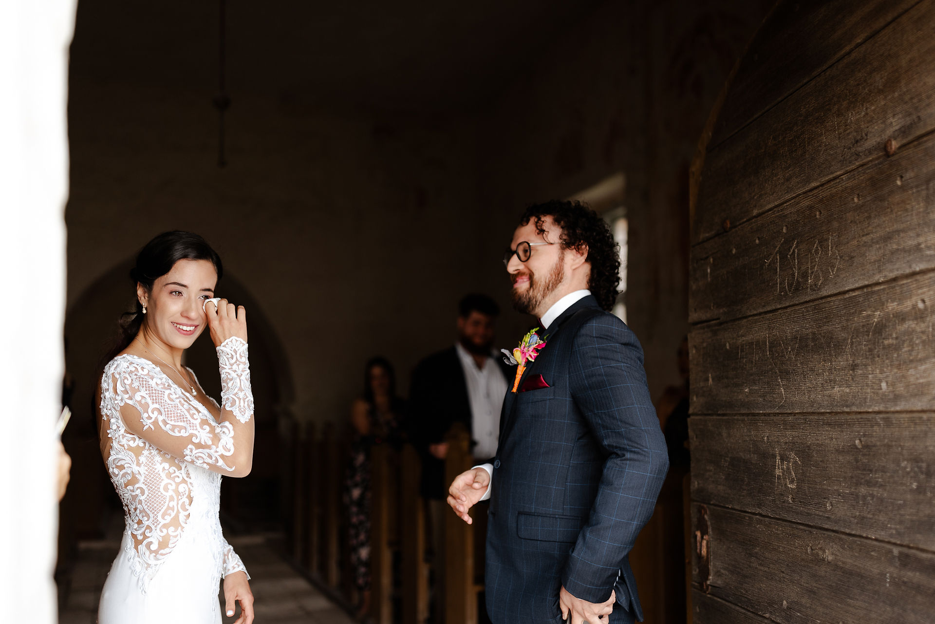 A candid moment of a bride wiping away a tear during an intimate wedding ceremony inside a historic stone building.