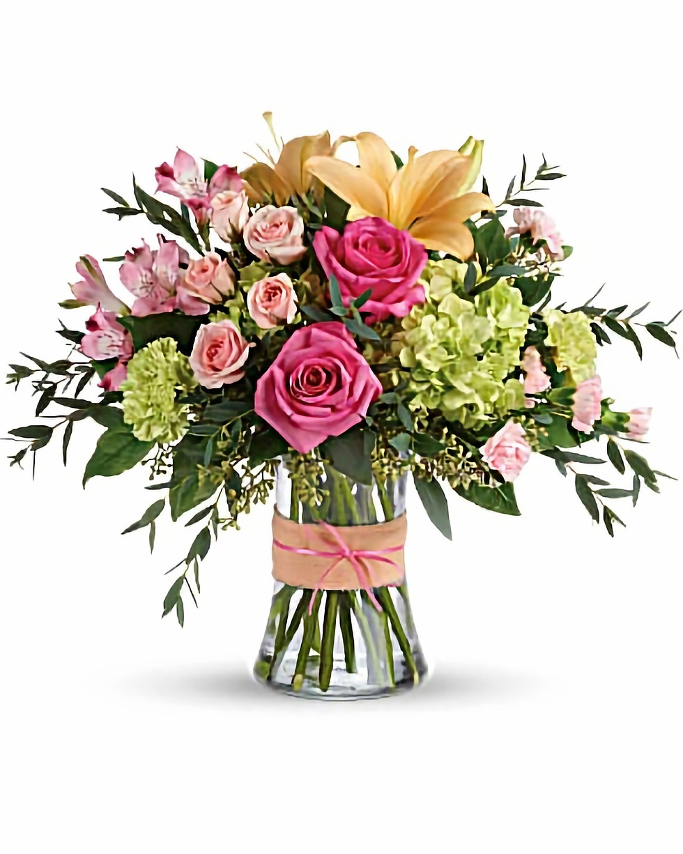 A selection of bright coloured spring flowers arranged in a tall glass vase.