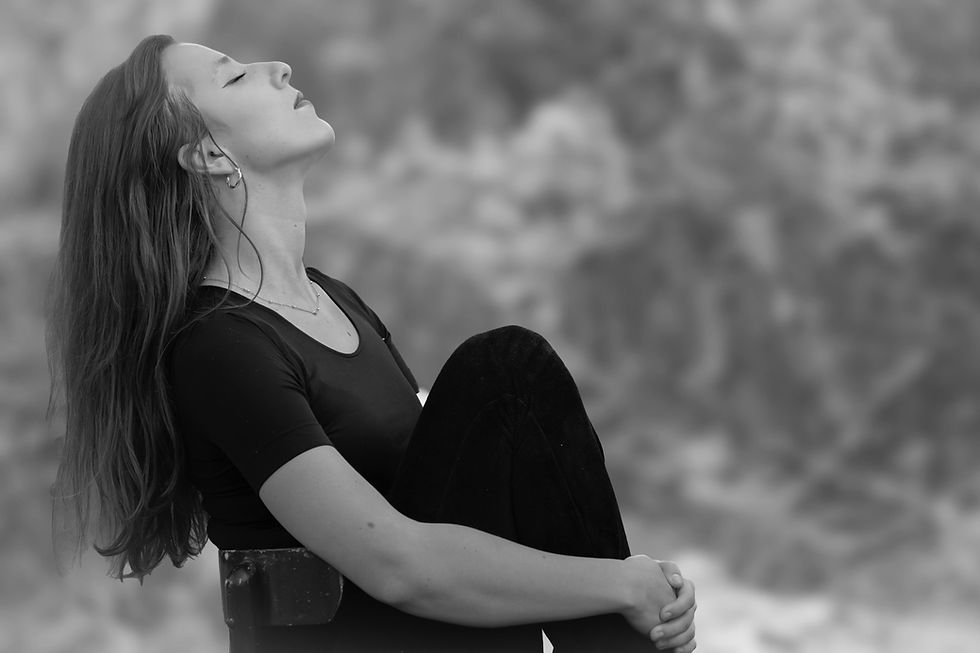 Black-and-white portrait of a woman with closed eyes, leaning back outdoors against a blurred background, looking calm and reflective