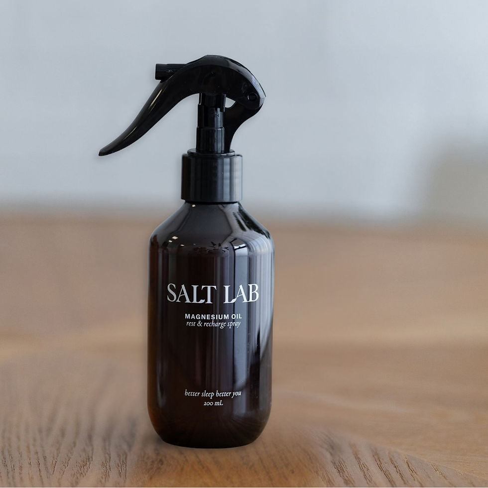 A brown spray bottle labeled Salt Lab Magnesium sits on a wooden surface with a blurred background.