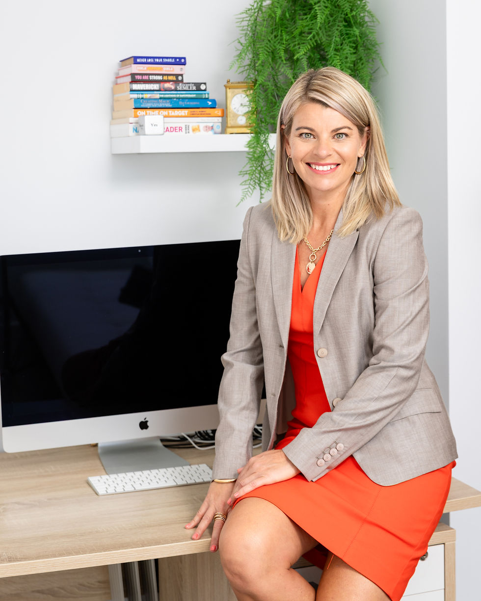 Smiling woman in business attire sits at a desk with computer.