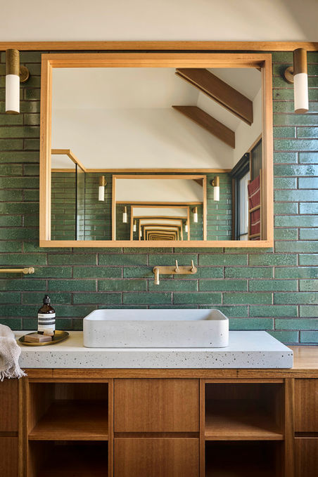 Modern bathroom vanity with a white sink, green tile walls, and a mirror reflecting a hallway with lights
