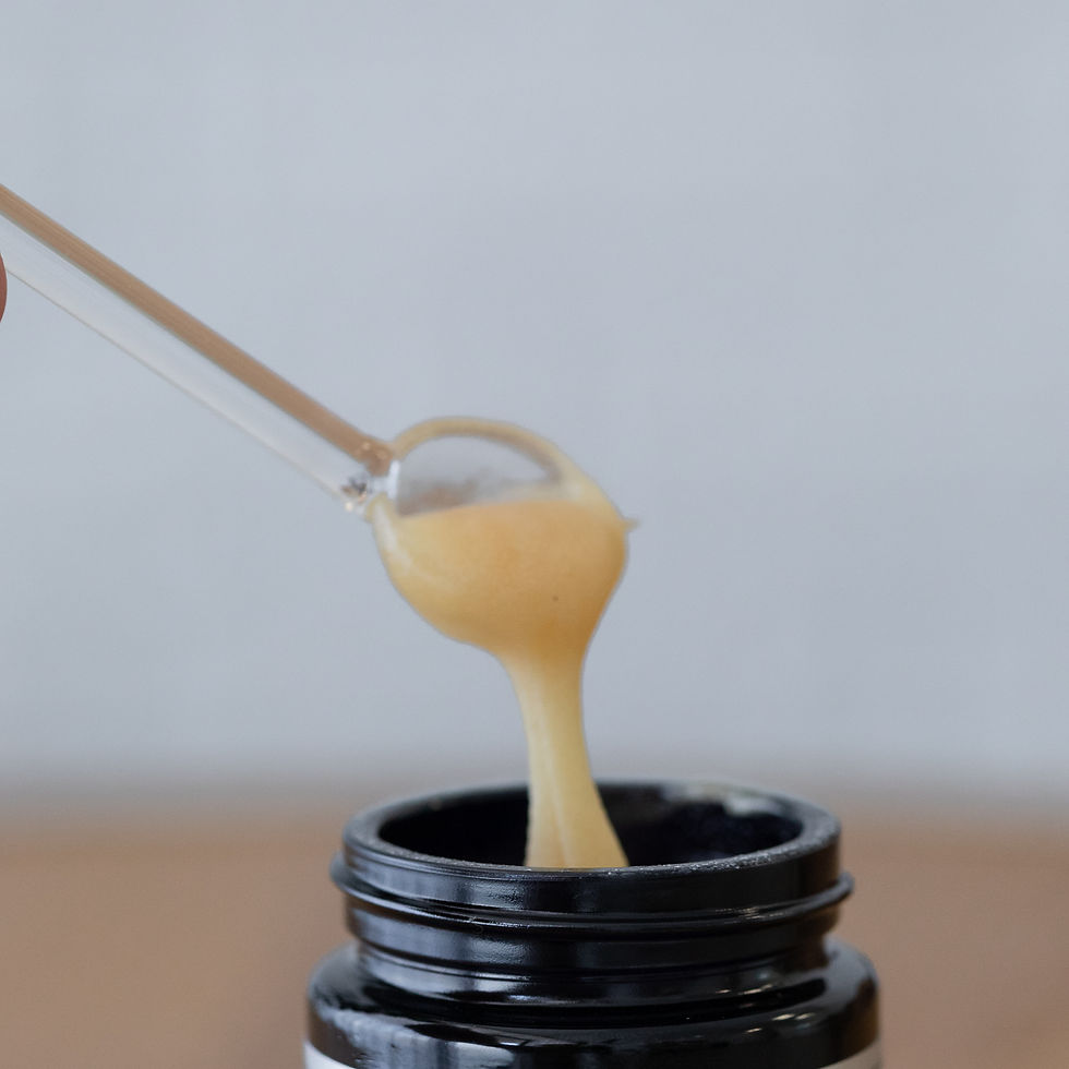 A spoon holding thick, yellowish paste being lifted from a black jar against a neutral background.
