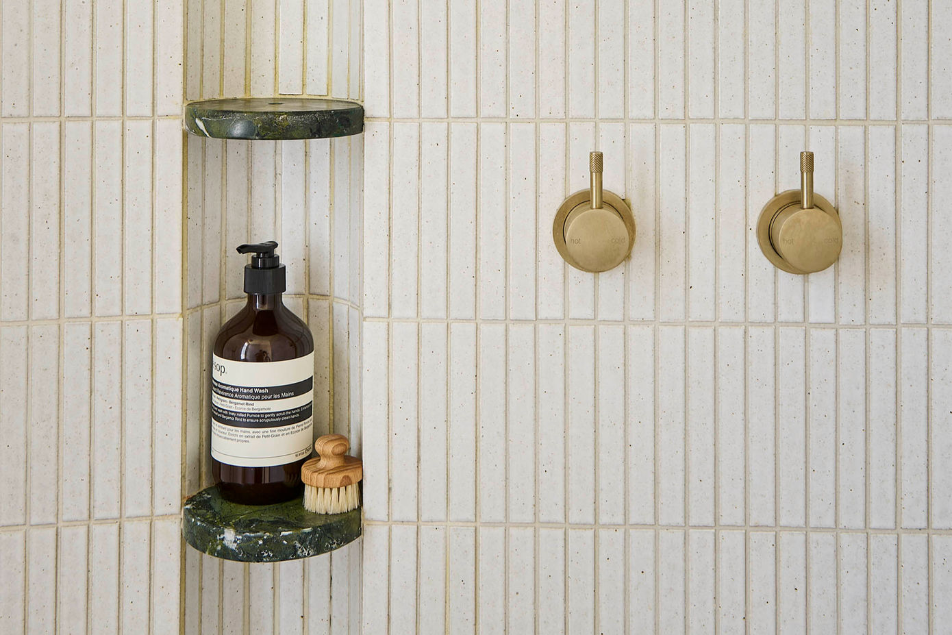 Shower with green marble shelves, a bottle of body wash, a brush, and two gold knobs