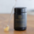 A black jar labeled Aurumaya Manna Gold sits next to a glass dropper containing a small amount of yellowish paste.