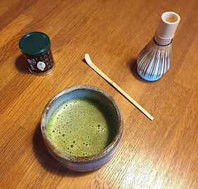 Matcha-Set auf Holztisch (Matchatee-Dose, Matchatee in Matcha-Schale / Chawan, Matcha-Löffel / Chashaku und Matcha-Besen / Chasen auf Matcha-Besenhalter / Kusenaoshi)