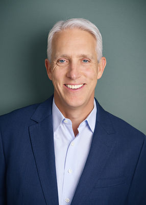Headshot of man with white hair and blue suit on green background.