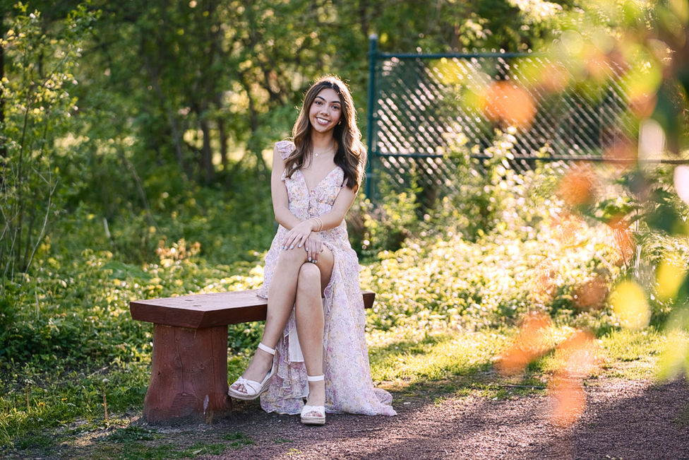 Senior Portrait of woman sitting on a bench in a green park at sunset. 