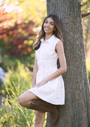 Senior Portrait of young woman in white dress and cowboy boots leaning on a tree at Keay Nature Center in Wilmette